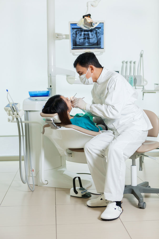 photo of male asian dentist diong a dental check up to a young asian woman in a dentist office